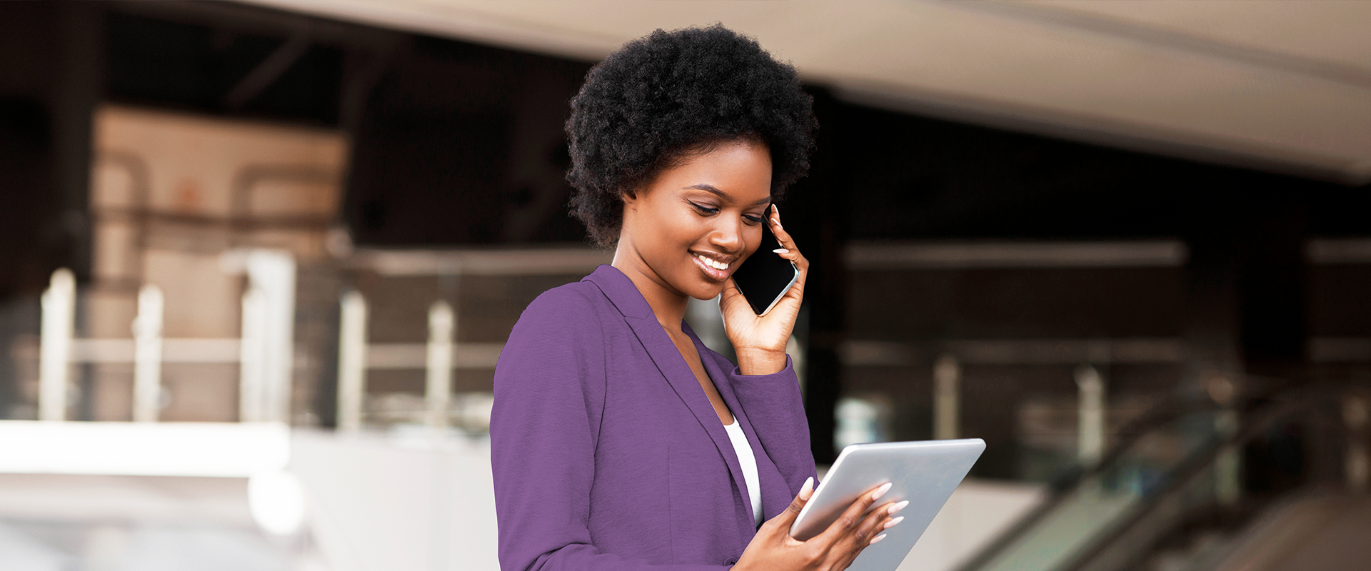 Mulher negra falando em um telefone celular equanto segura um tablet